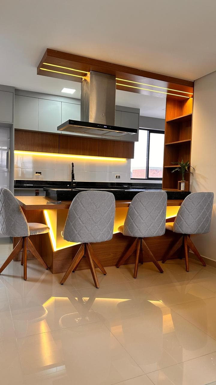 Bancada de cozinha com banquetas, iluminação integrada e armários ao fundo