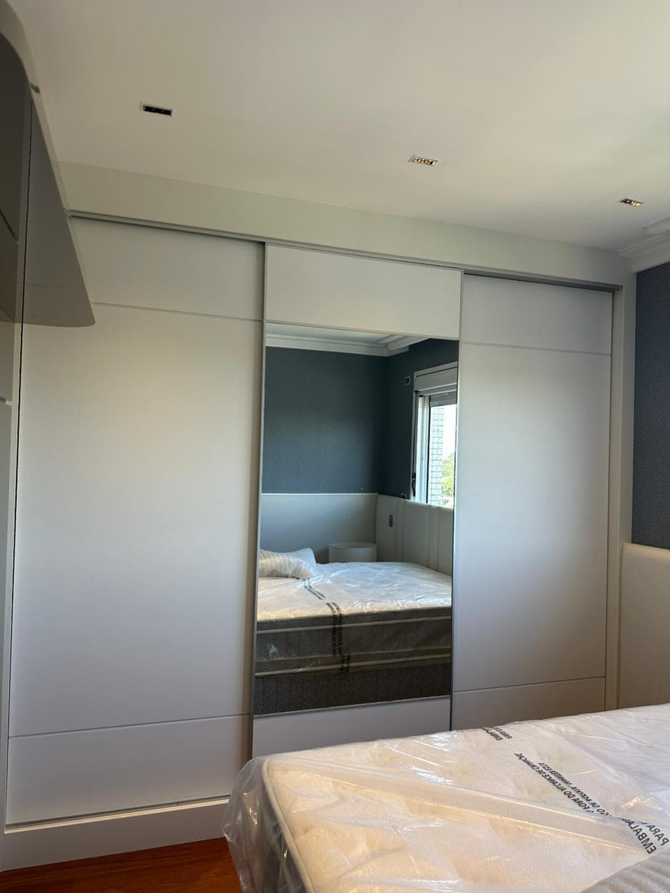 Guarda-roupa claro com três portas de correr e espelho na porta central